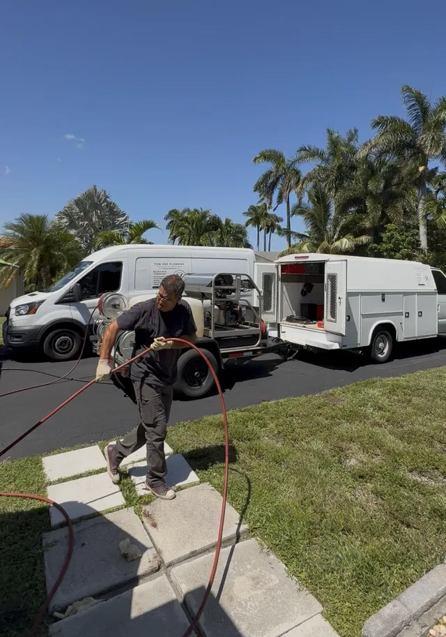 Tier One technician working beside two white Tier One service trucks in a South Florida driveway